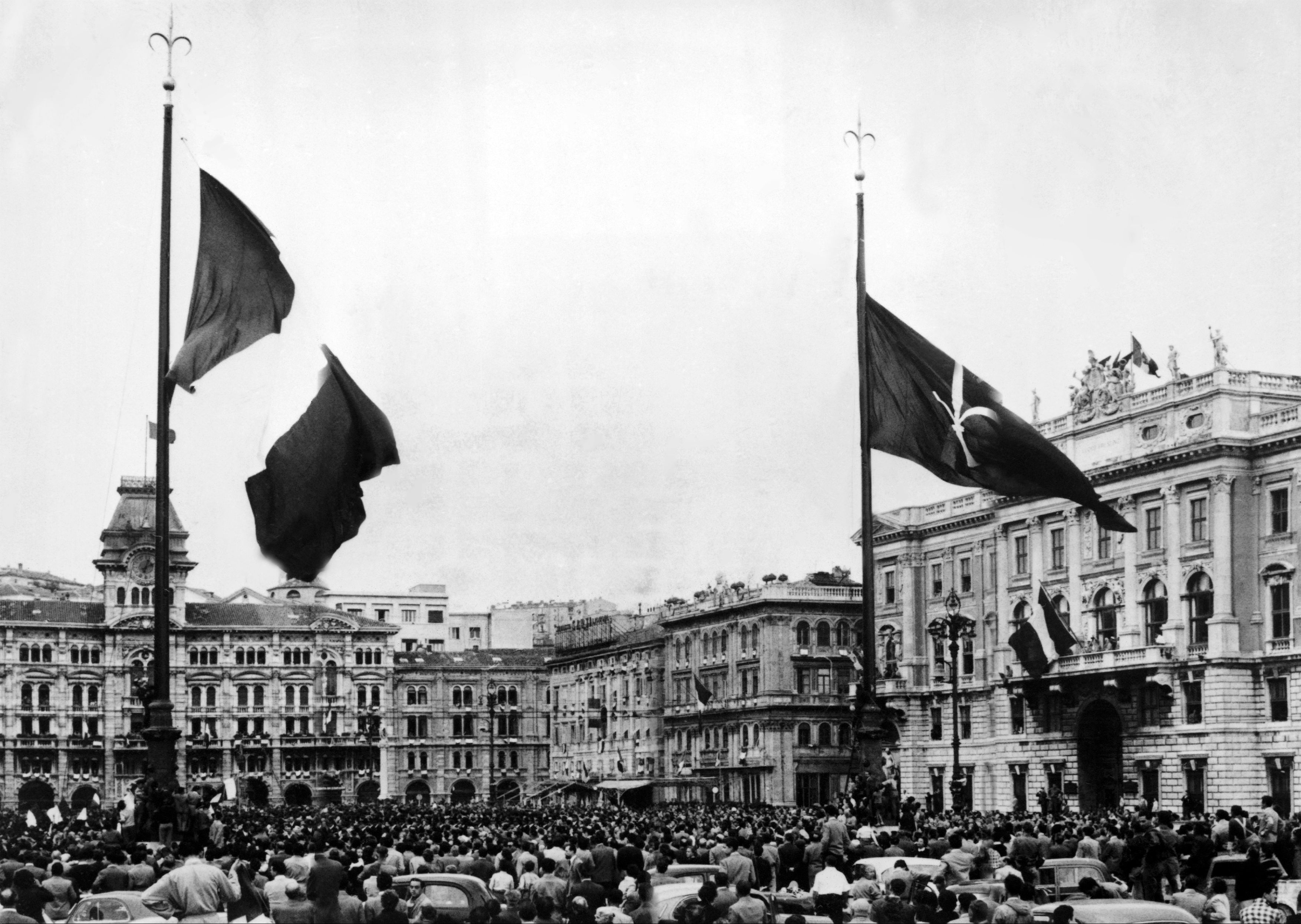 In piazza dell'Unità una folla innumerevole è presente per assistere all'alzabandiera della bandiera italiana (a sinistra) e della bandiera di Trieste 