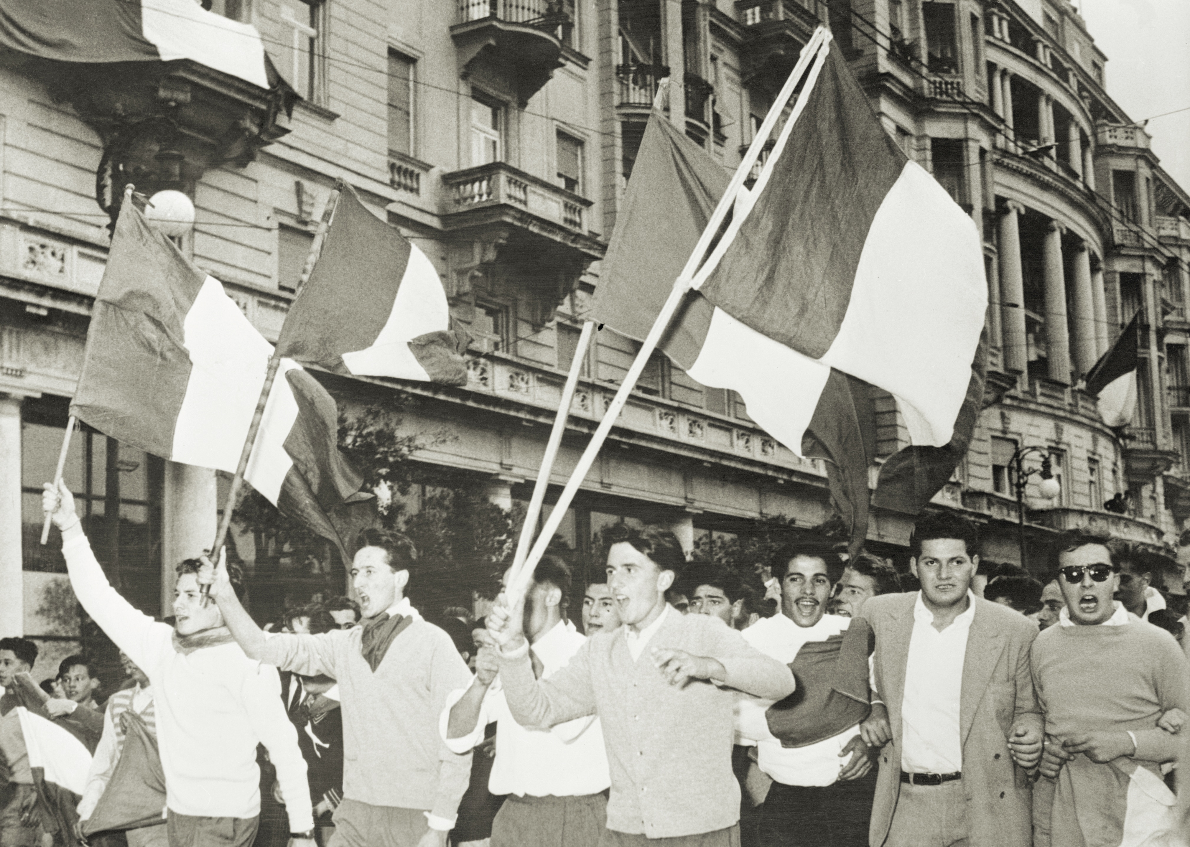 I cittadini entusiasti di Trieste marciano con le bandiere italiane attraverso Piazza dell'Unità durante la cerimonia di innalzamento della bandiera italiana sulla città per la prima volta dalla Seconda Guerra Mondiale